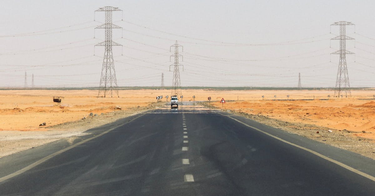 A solitary road stretches through the desert with power lines and a car on the horizon.