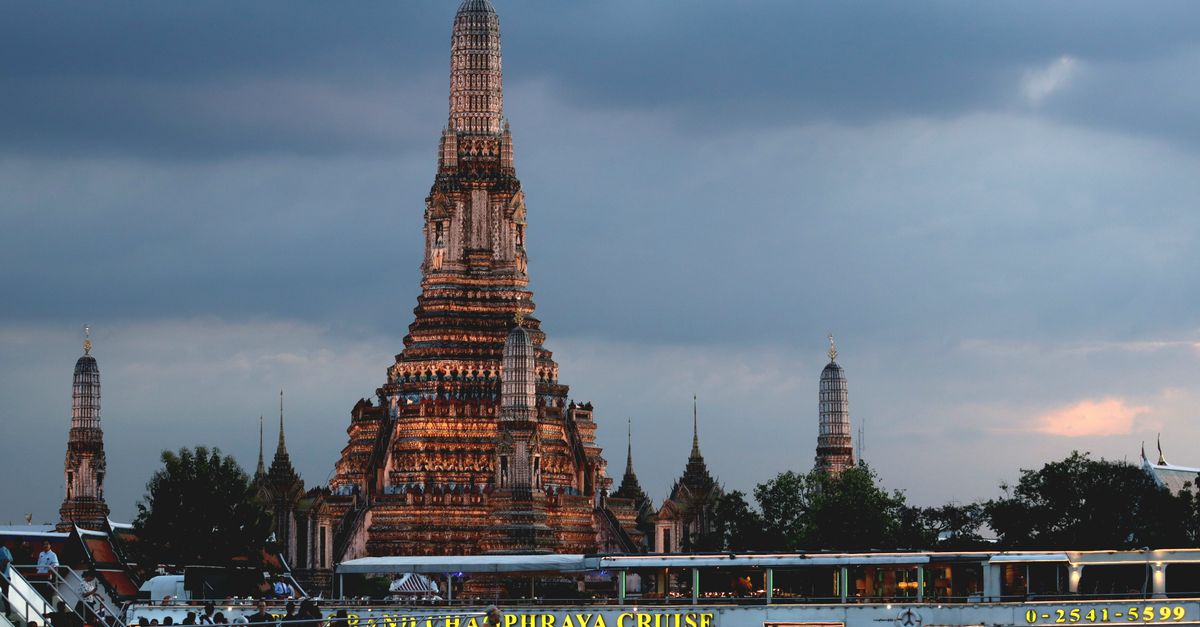 Stunning view of Wat Arun temple with cruise boat on Chao Phraya River at sunset in Bangkok, Thailand.