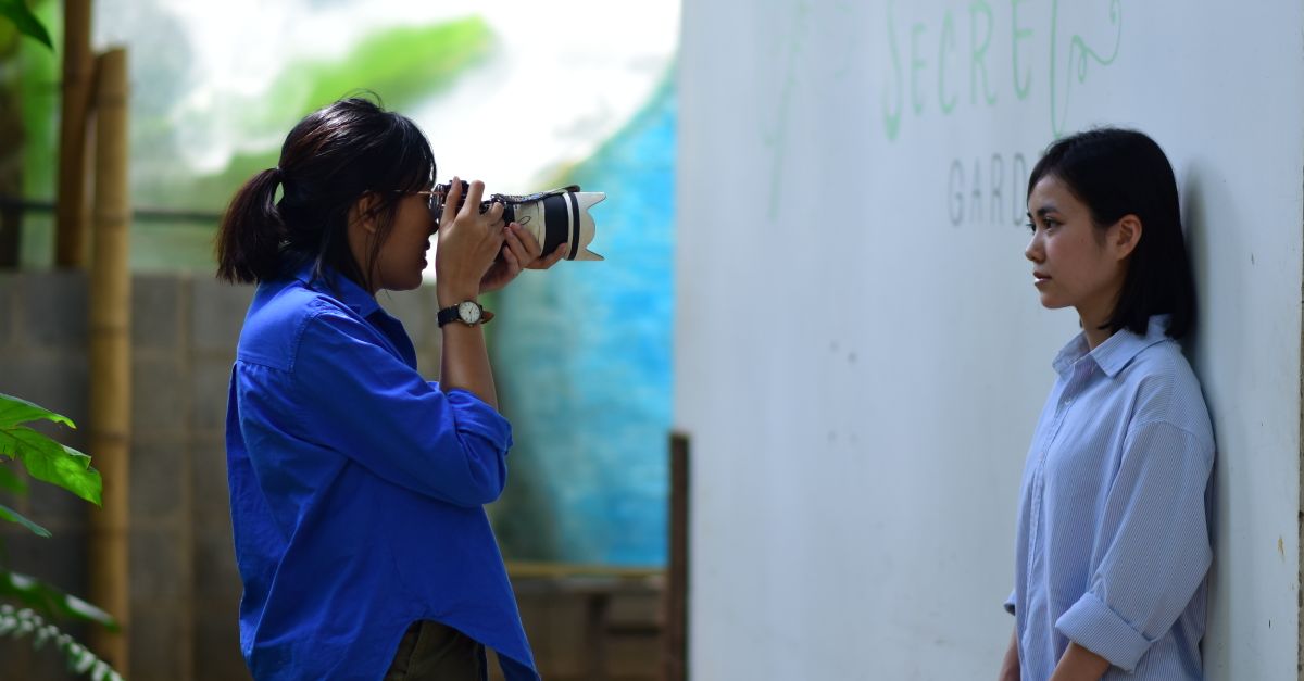 A photographer takes a portrait of a woman in an outdoor setting with a "Secret Garden" backdrop.