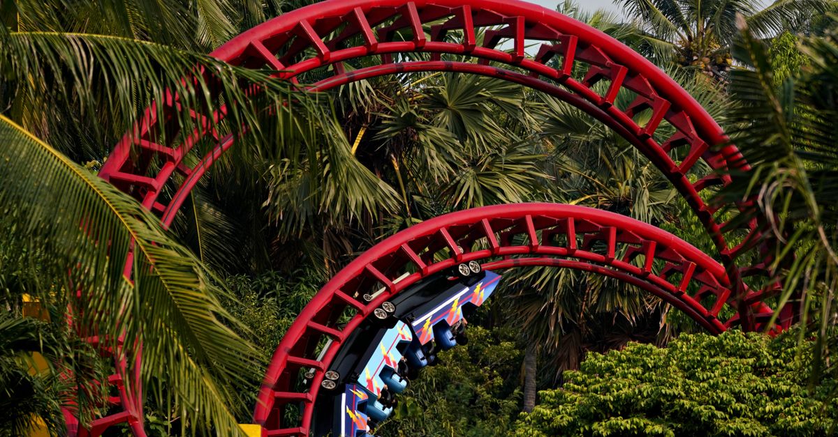 Colorful roller coaster loops through lush palm trees on a sunny day.
