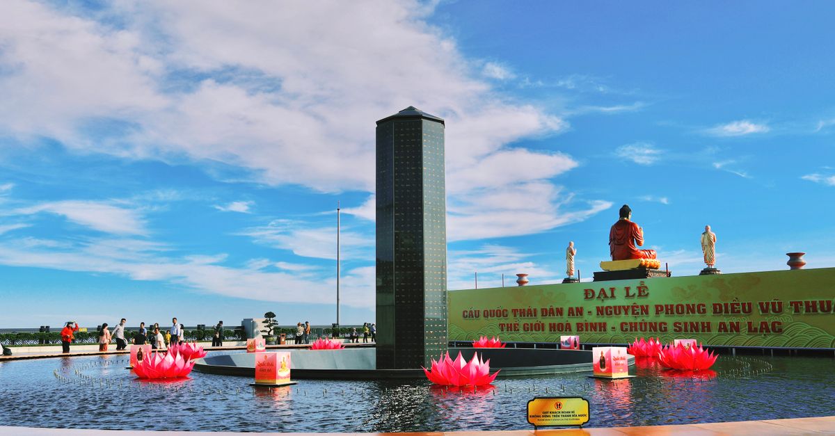 Colorful outdoor view of Ba Den Mountain with lotus pond and statues under a bright sky.