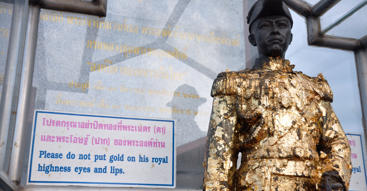 Golden statue in Thailand with sign requesting not to cover eyes and lips. Cultural respect imagery.