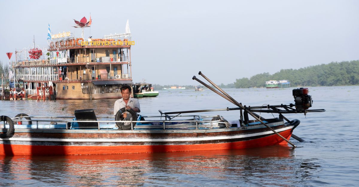 A traditional wooden boat with a local man on the Mekong River in Cần Thơ, Vietnam.