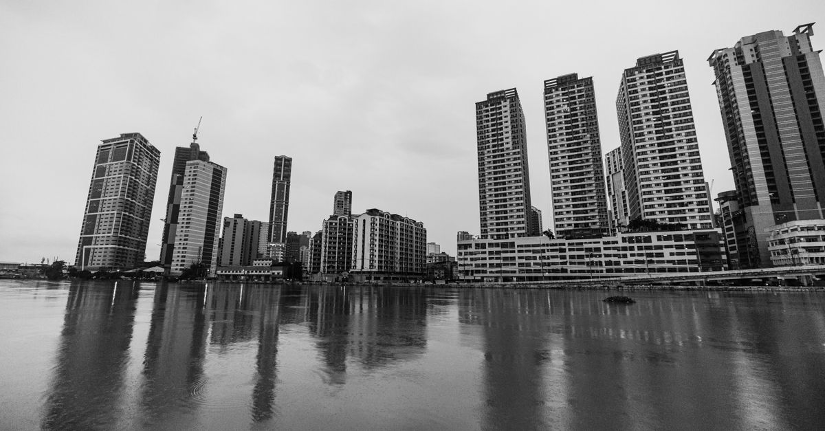 A serene black and white view of modern high-rise buildings reflecting over calm water.
