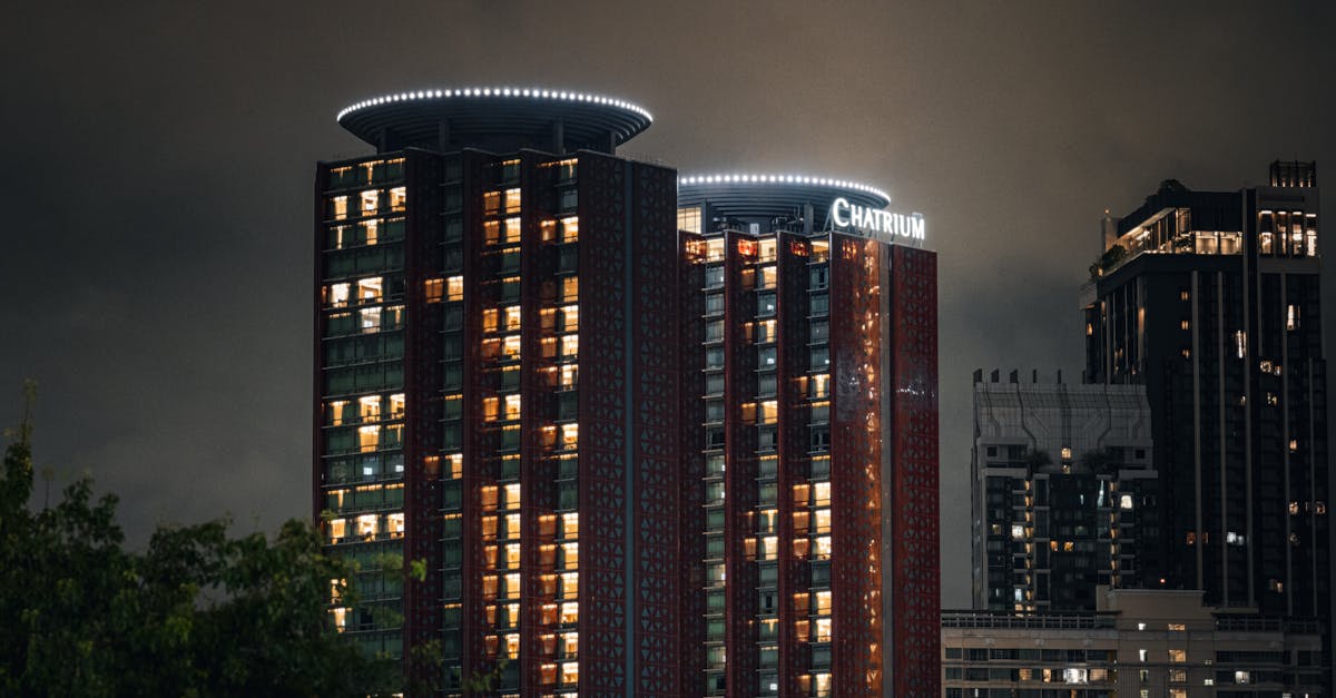 Illuminated Chatrium Hotel in Bangkok skyline at night, showcasing modern architecture.