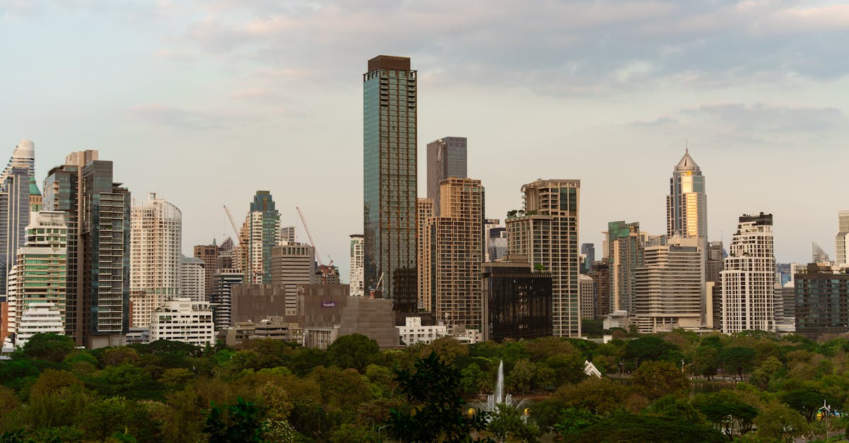 Explore the vibrant skyline of Bangkok with modern skyscrapers at dusk, featuring lush greenery in the foreground.
