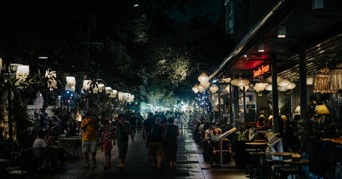 A lively nighttime street scene with people enjoying a bustling outdoor cafe under colorful lights.