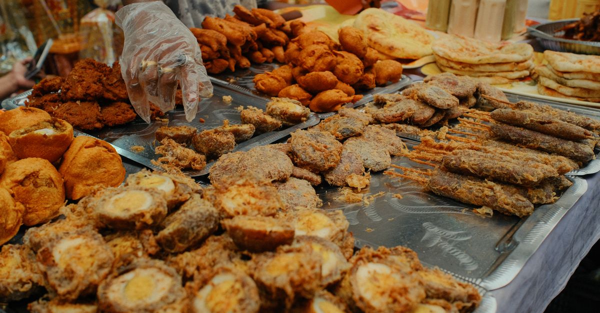 A variety of traditional foods displayed at a bustling Dhaka Iftar market during Ramadan.