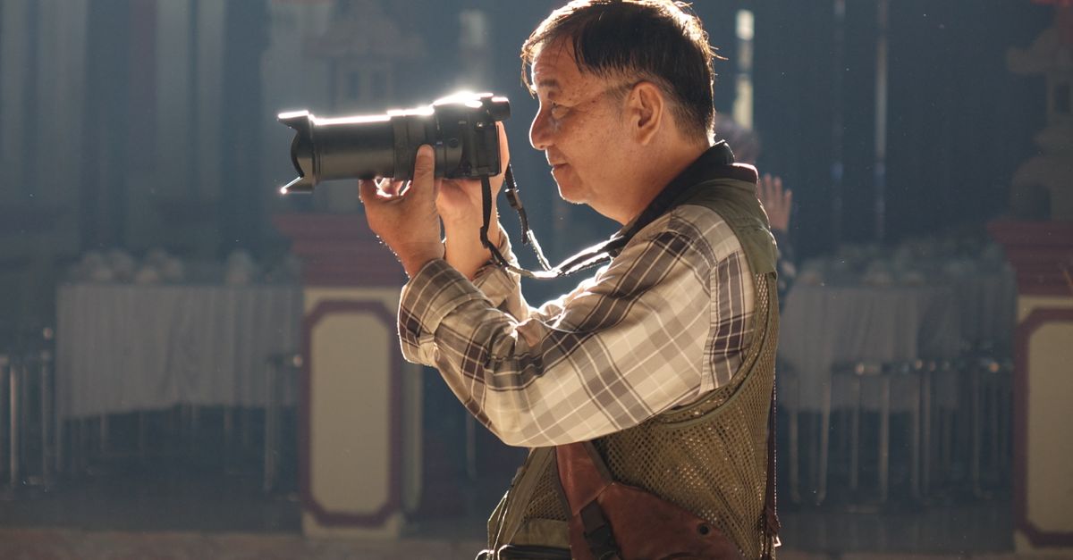 An elderly man taking photos indoors with a DSLR camera, highlighting passion for photography.