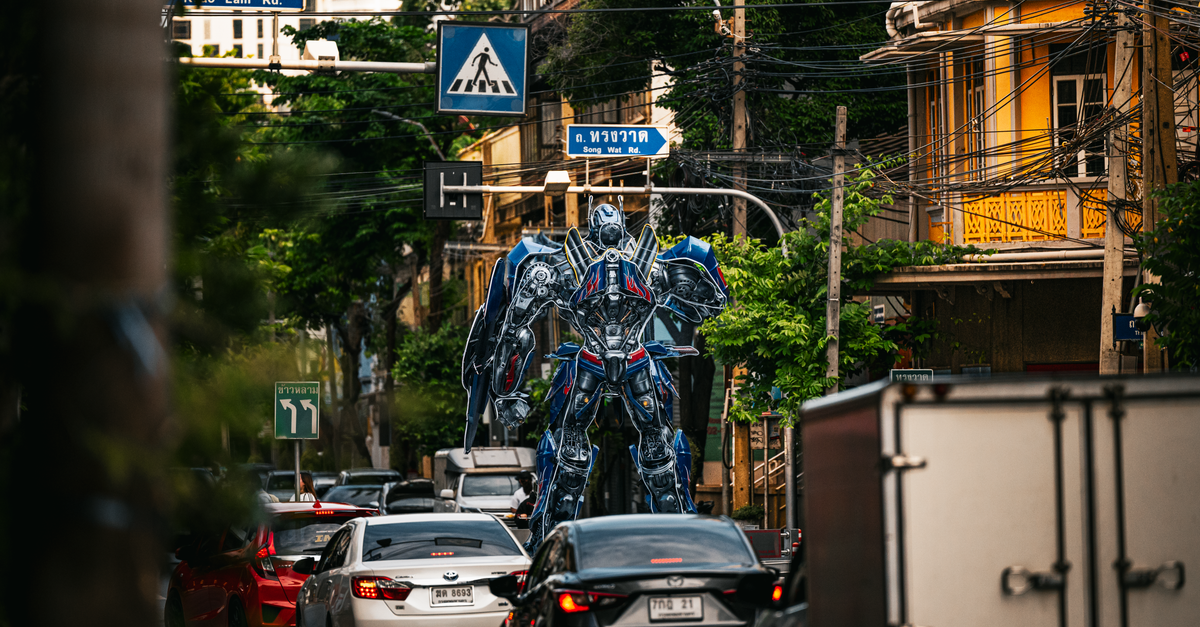 A towering robot statue stands amidst bustling traffic on a street in Bangkok, Thailand.