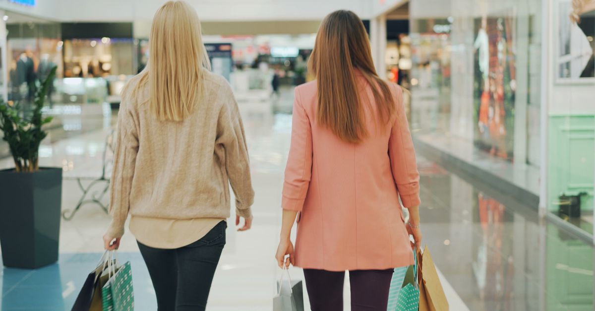 Two women walking in a mall holding shopping bags, back view.