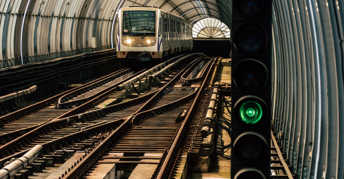 A train approaching through a modern steel tunnel with green light signal, showcasing urban transit.