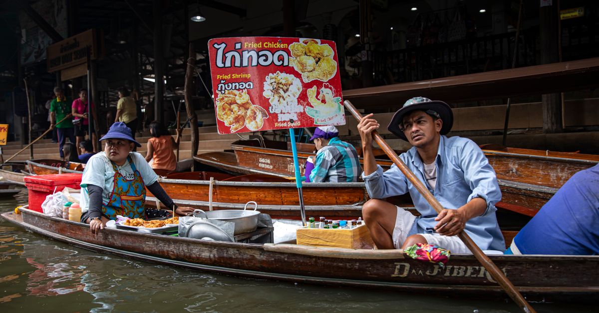 Two vendors at a floating market selling fried chicken and shrimp from their boats.