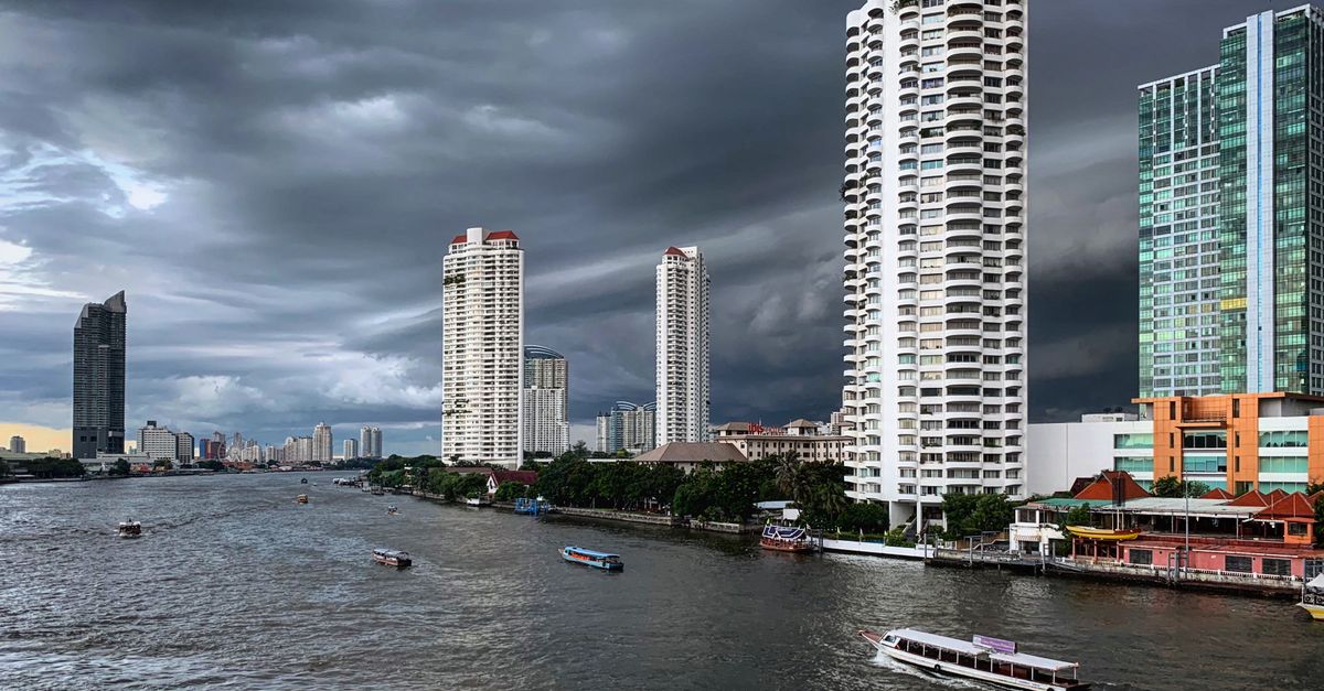 Dramatic view of Bangkok's skyscrapers along the Chao Phraya River under a stormy sky.
