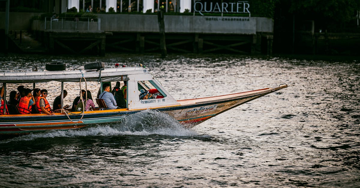 A vibrant longtail boat carrying passengers on the Chao Phraya River with a cityscape backdrop.