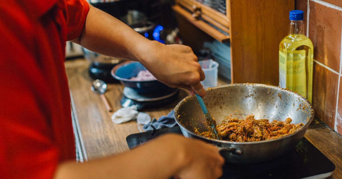 Person cooking shredded meat in a wok on a stove, home kitchen cooking scene.