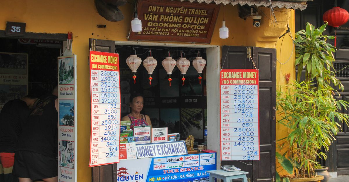Currency exchange booth in Đà Nẵng, Vietnam, displaying exchange rates. A woman stands inside the office.
