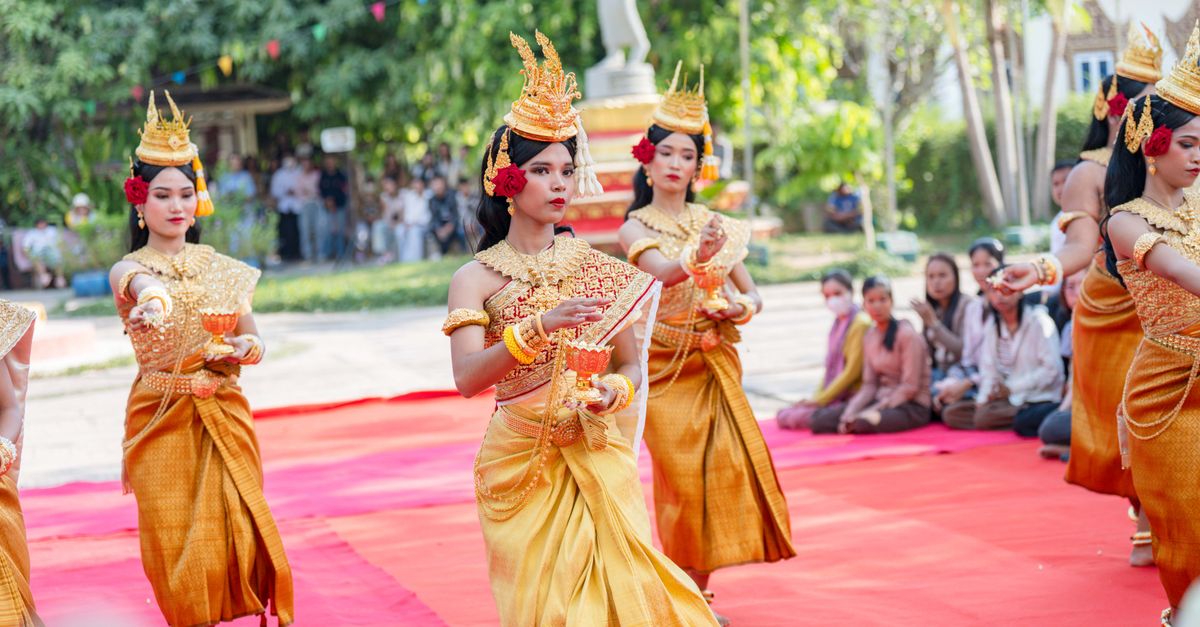 Colorful traditional Cambodian dance performance with women in elegant costumes on red carpet outdoors.