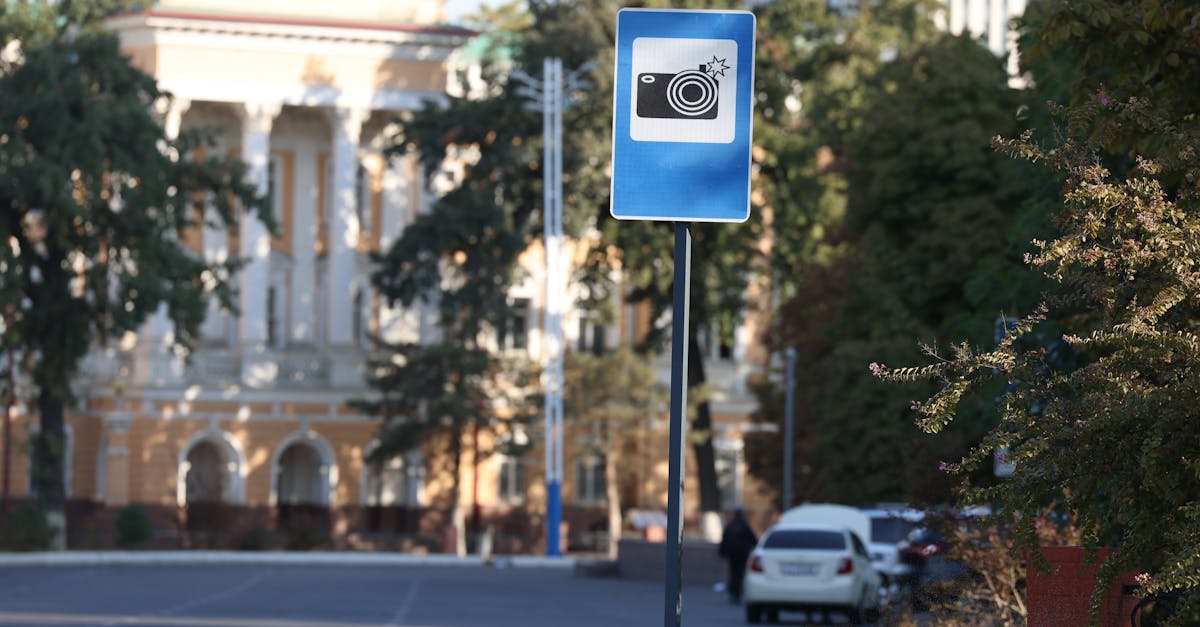 A blue traffic camera warning sign on a city street with blurred buildings in the background.