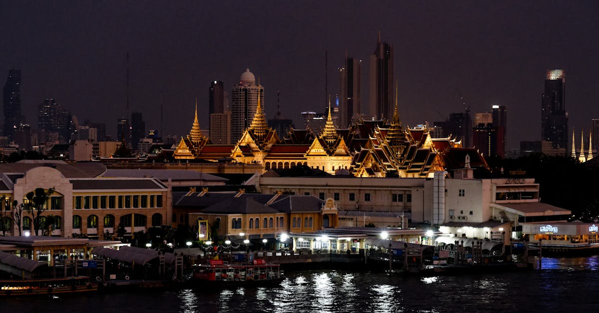 Illuminated Grand Palace with Bangkok skyline at night, depicting vibrant city life.