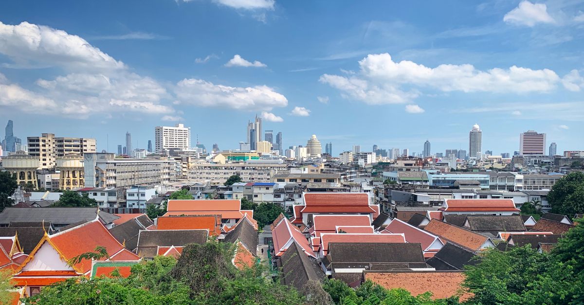 Panoramic view of Bangkok skyline featuring traditional Thai rooftops against a modern cityscape.