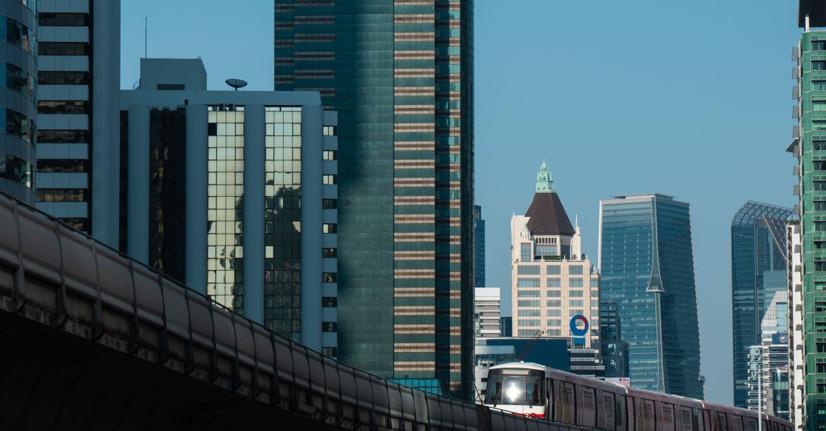 MRT train passing through Bangkok's modern skyline, showcasing skyscrapers and urban architecture.