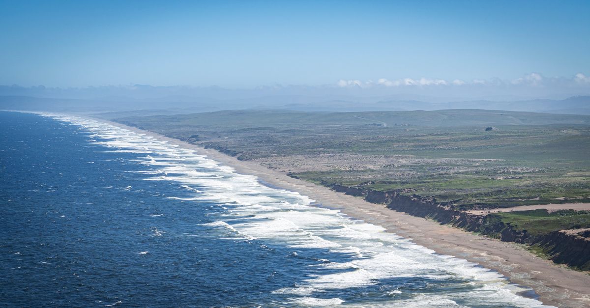 A breathtaking aerial view of a vast coastline with crashing ocean waves and clear blue skies.