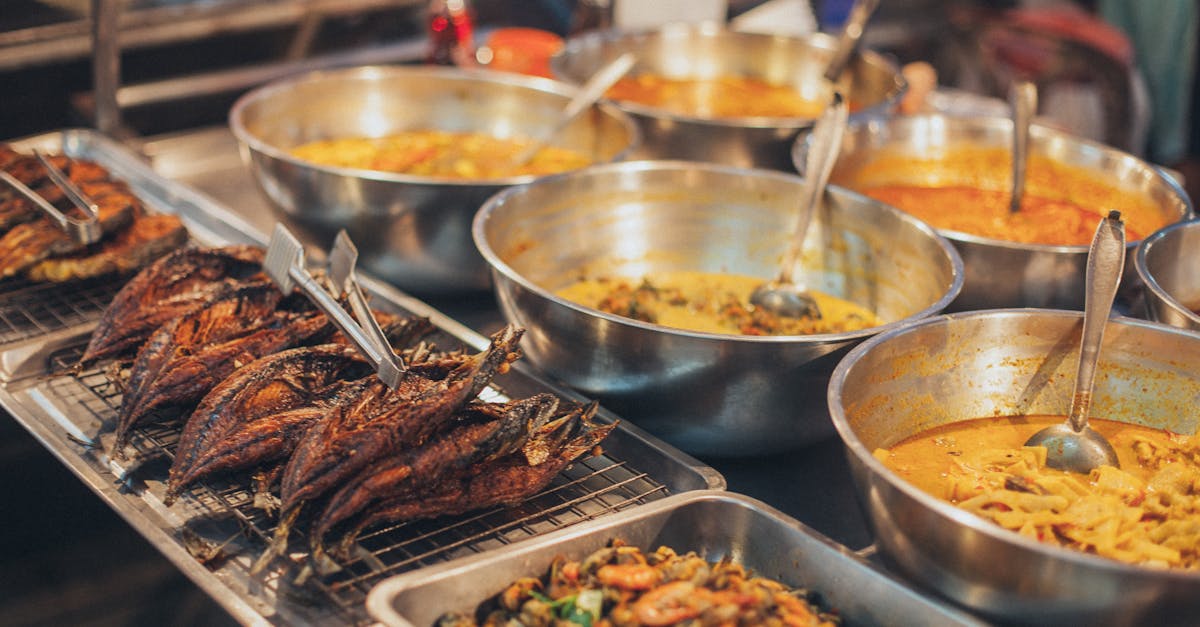 A colorful array of Asian street food dishes in metal bowls on display, showcasing diverse flavors.