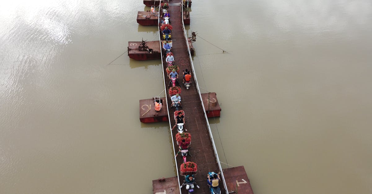 Drone view of people on motorcycles transporting goods in baskets for sale in market while moving on floating bridge across river