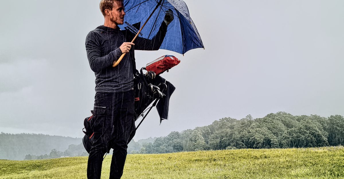 Golf player holding an umbrella while standing on a rainy golf course in Sweden.