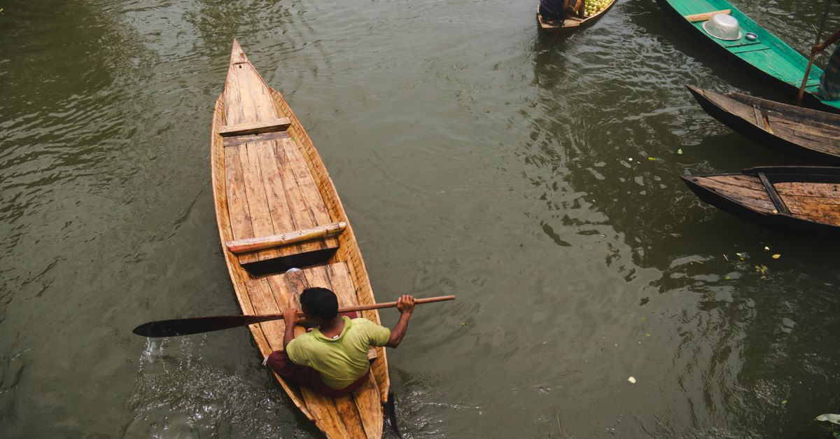 From above of faceless ethnic male in t shirt using paddle while swimming through river on wooden canoe in daytime