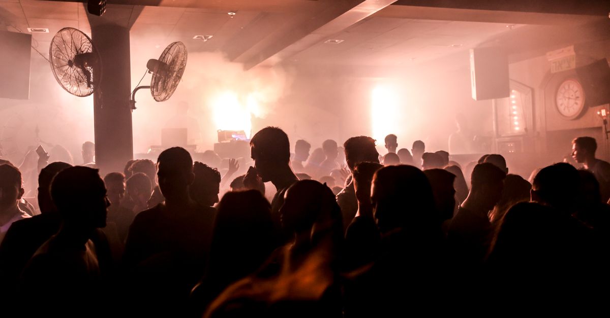Silhouetted crowd dancing in a smoky nightclub with vibrant lights.