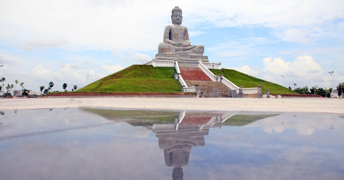 Magnificent Buddha statue atop a hill, perfectly reflected in calm water.