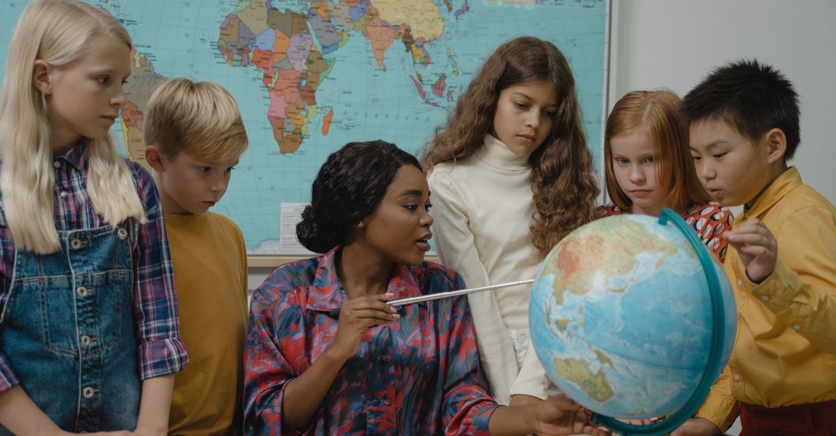 Diverse elementary students learning geography with a teacher and globe in the classroom.
