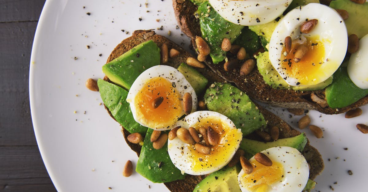 Delicious avocado toast topped with soft-boiled eggs and pine nuts on a white plate.