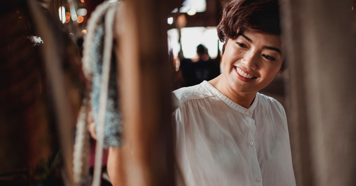 Crop content Asian female wearing white blouse looking with smile in souvenir or clothes store in local street market