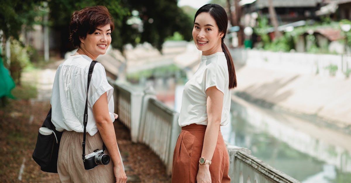 Back view of young cheerful ethnic female friends in casual wear looking at camera over shoulder near water channel in summer
