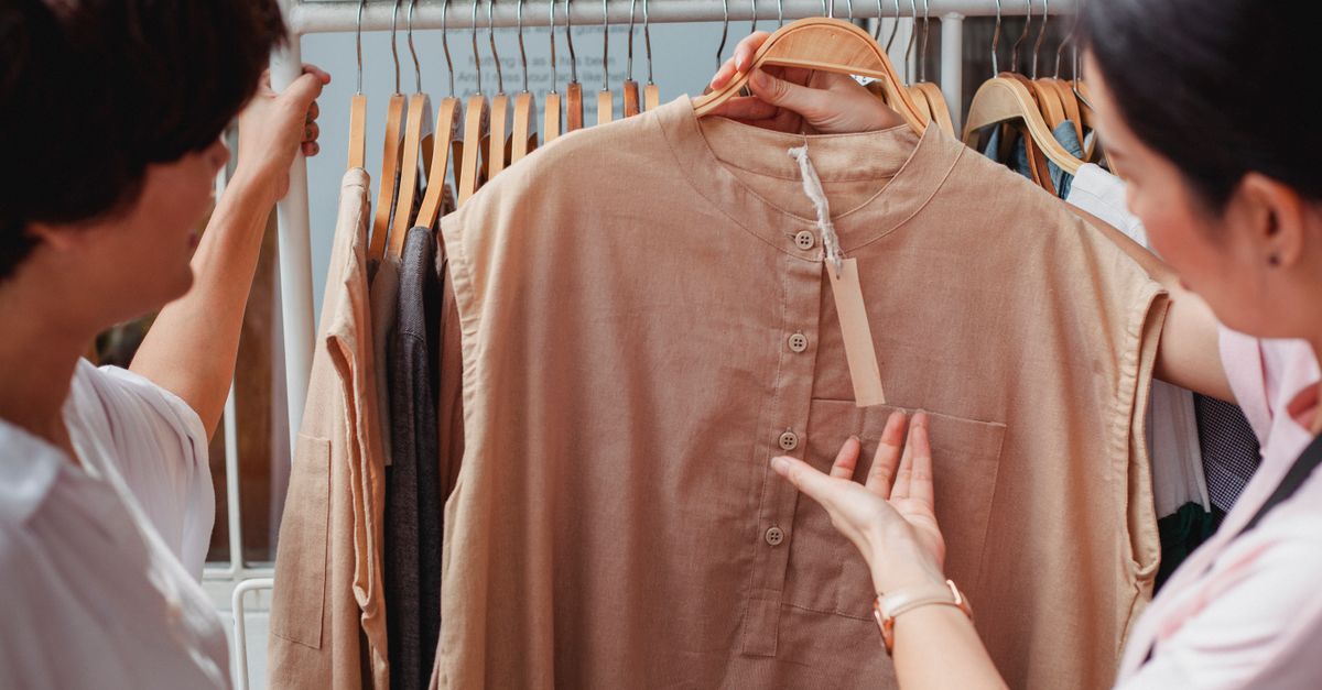 Side view of crop anonymous ethnic female buyers talking while watching apparel with price tag near rack