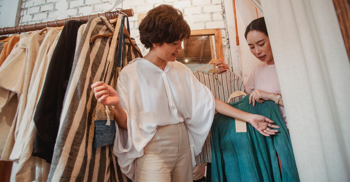 Low angle of stylish young ethnic female friends in trendy outfits choosing clothes in fashion boutique