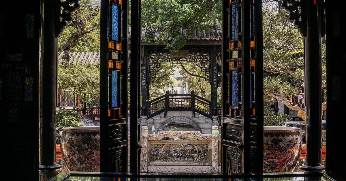 View through ornate doorway to traditional architecture and greenery in Guangzhou park.
