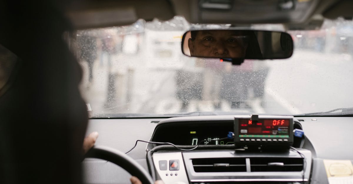 Back view of man reflecting in mirror while driving along street in city on urban background in soft daylight