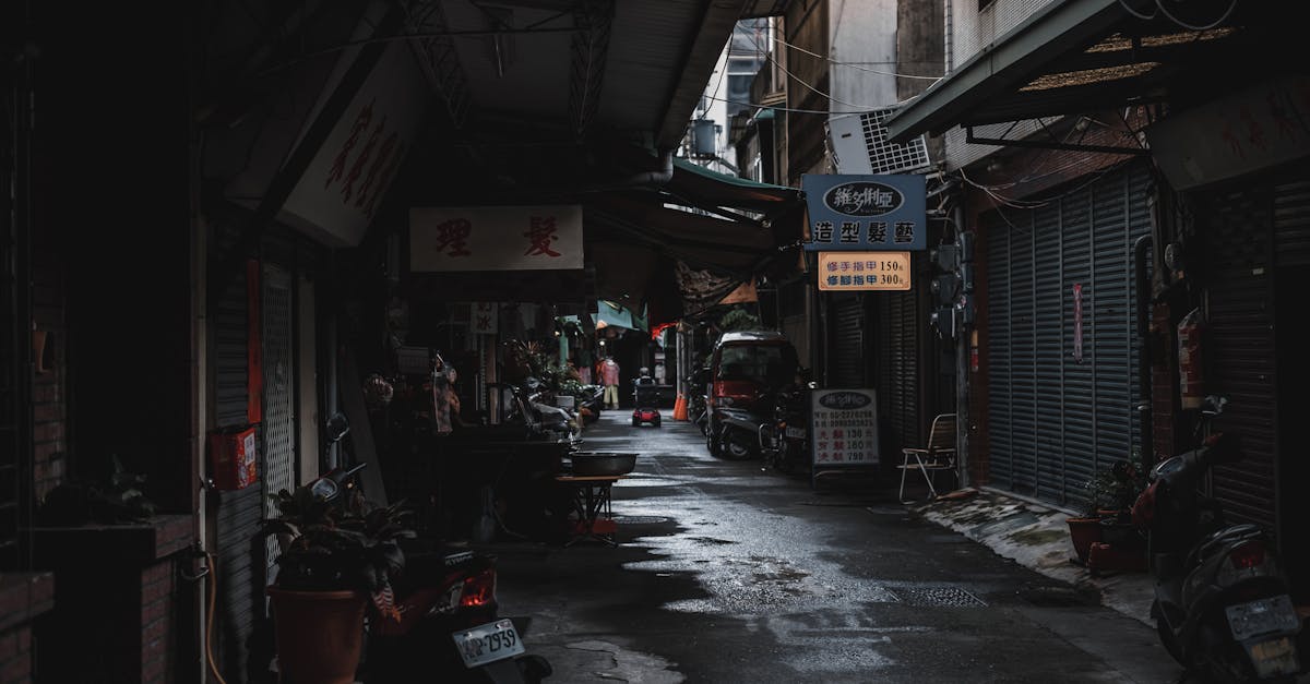 Narrow moody alley in an Asian city with wet roads and dim lighting.