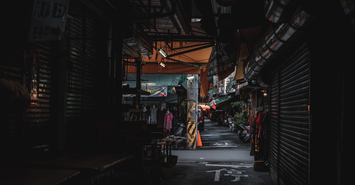A dimly lit urban street market at twilight with closed shops and moody atmosphere.