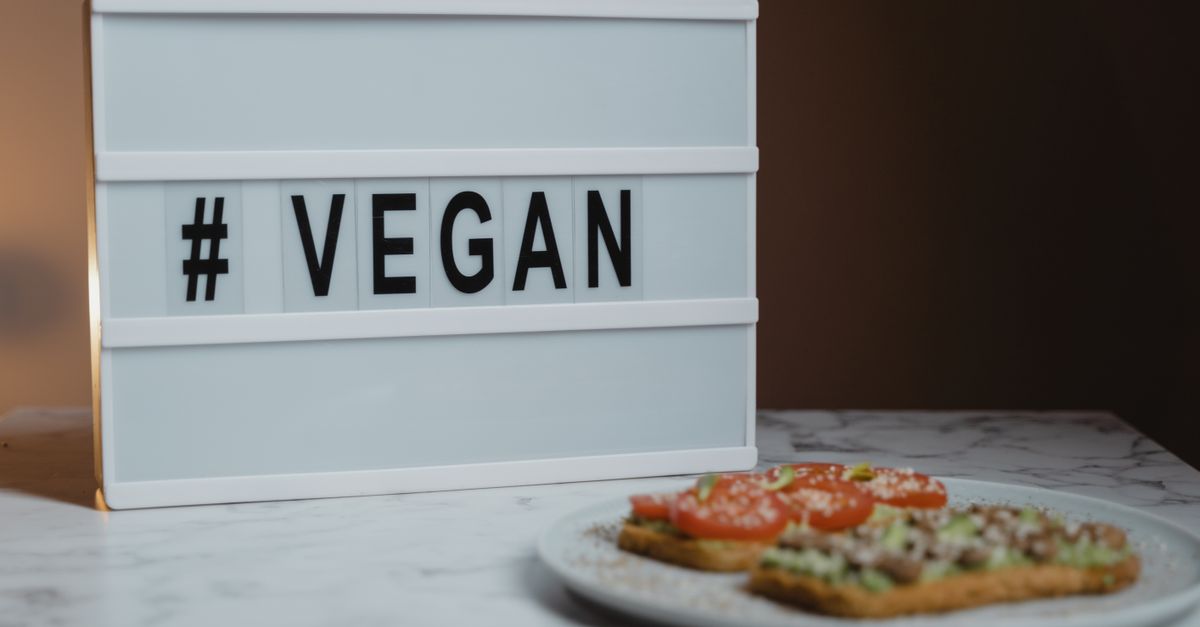 Stylish lightbox displaying '#VEGAN' beside a plate of avocado toast on a marble surface.