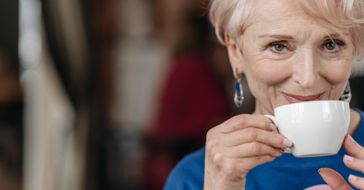 Close-up of a senior woman enjoying a hot drink, indoors, smiling warmly.