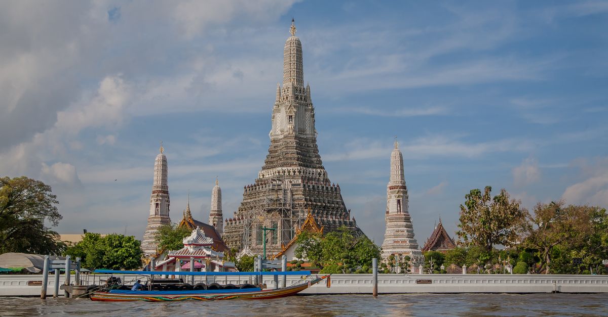 Explore the iconic Wat Arun temple along the Chao Phraya River in Bangkok under a vibrant sky.