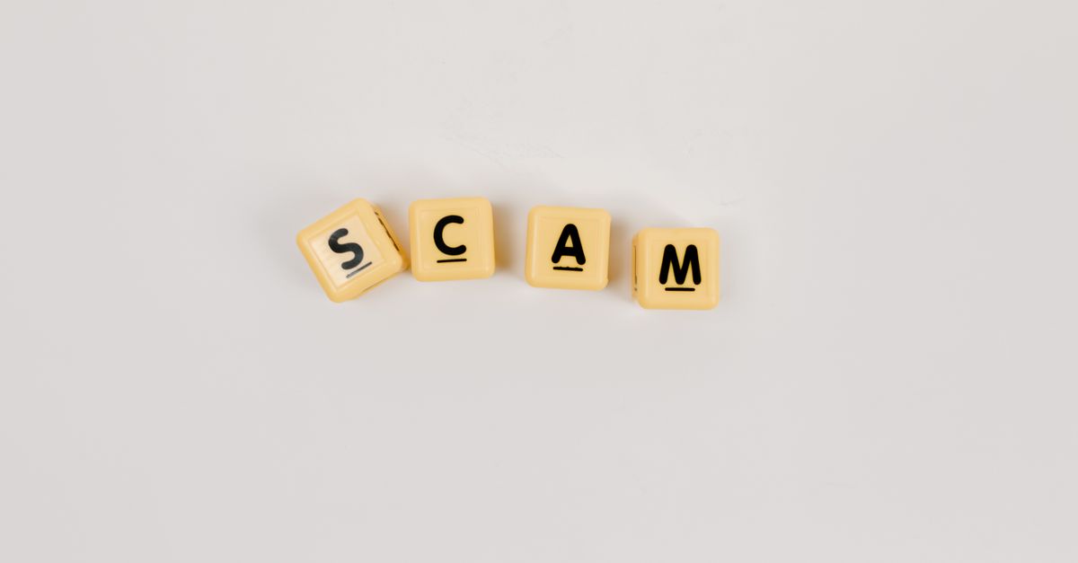 Four Scrabble tiles forming the word 'SCAM' on a neutral background, highlighting concepts like deceit.