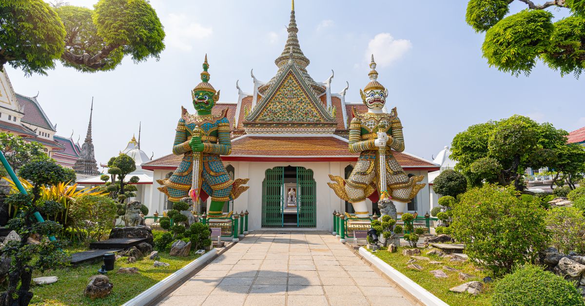 Stunning view of guardian statues at Wat Arun temple in Bangkok, Thailand, showcasing intricate Thai architecture.