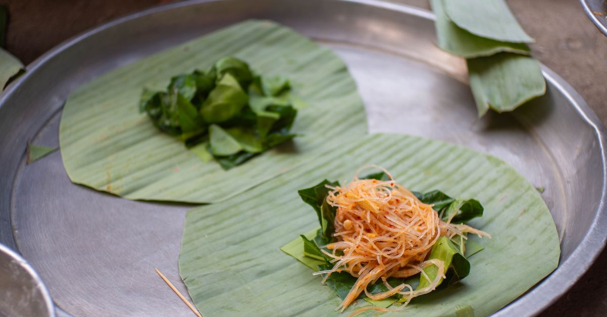 Close-up of a leaf-wrapped dish with vegetables and shredded ingredients on a stainless tray.