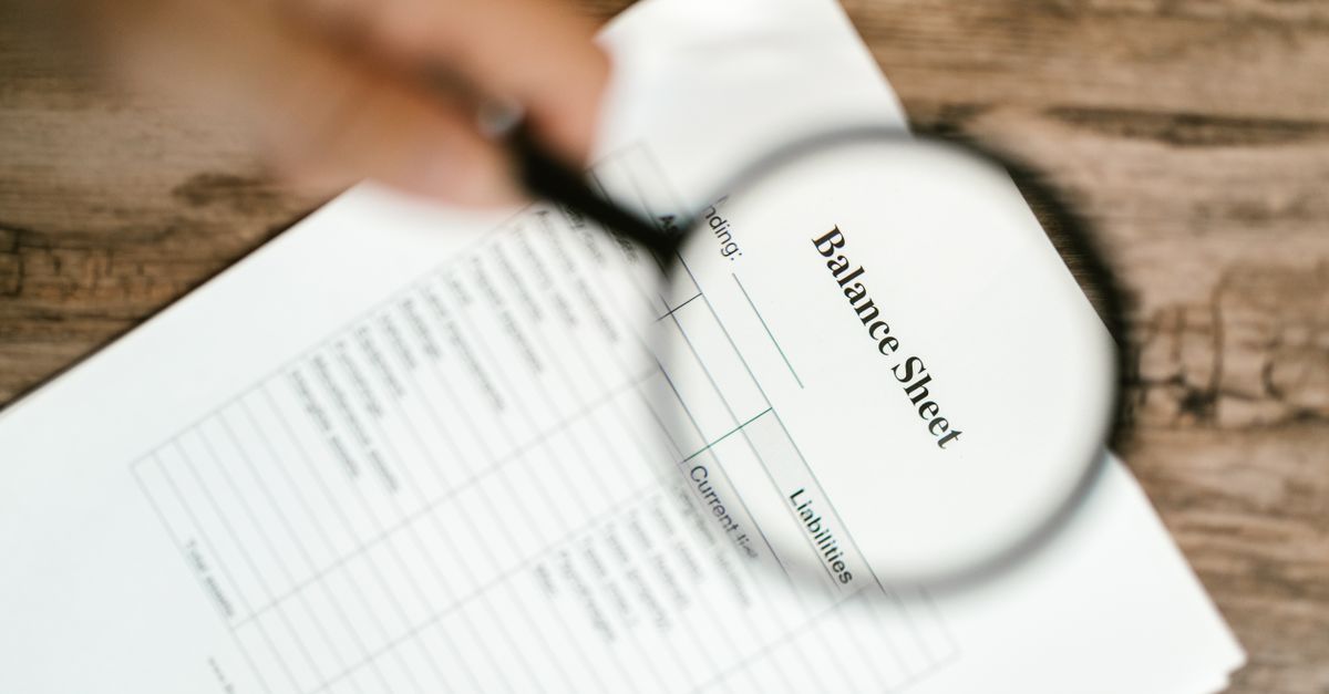 Close-up of a balance sheet under a magnifying glass on a wooden table.
